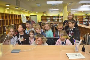 Dzieci za ladą biblioteczną obserwują bibliotekarkę podczas zamawiania książek