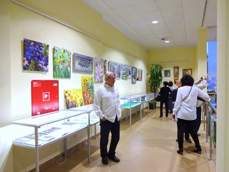 Obrazy prezentowane na wystawie, gabloty wystawiennicze oraz kilka osób w galerii