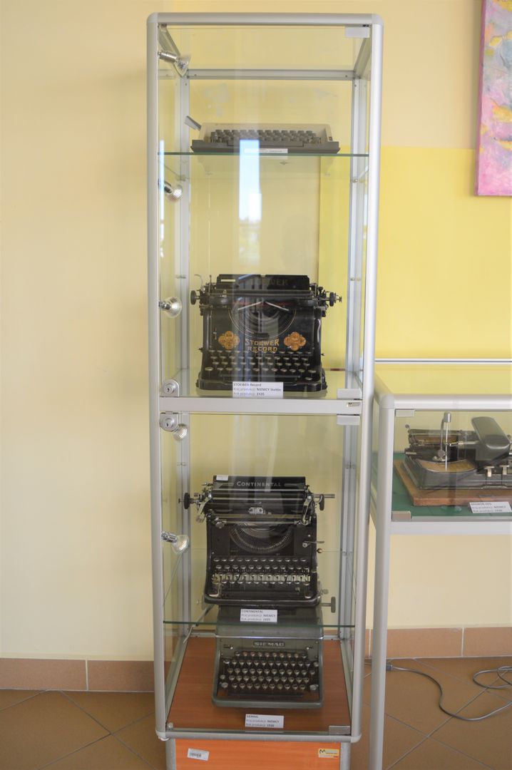 Zdjęcie przedstawia gablotę z czterema zabytkowymi maszynami do pisania 