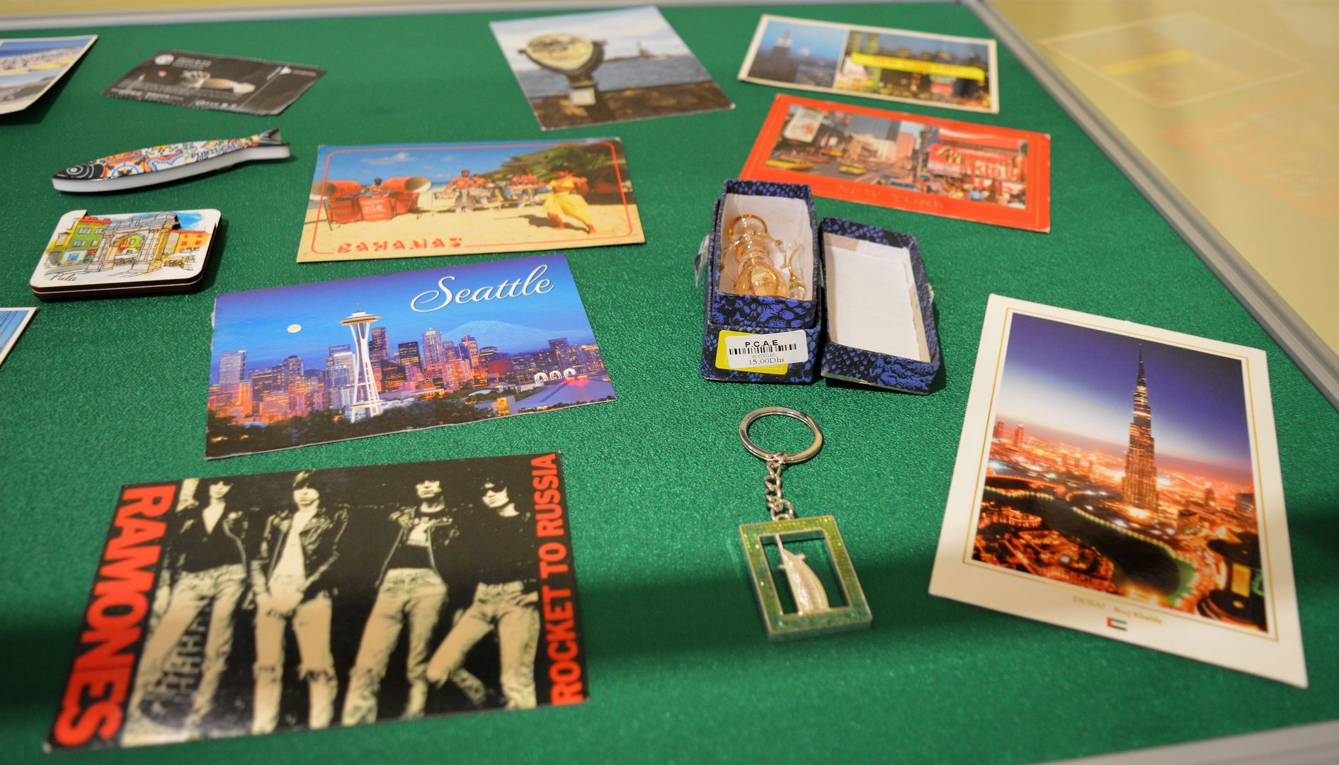 Zdjęcie przedstawia fragment gabloty wystawienniczej z pocztówkami, madnesami i innymi pamiątkami z podróży pracowników Biblioteki Głównej
