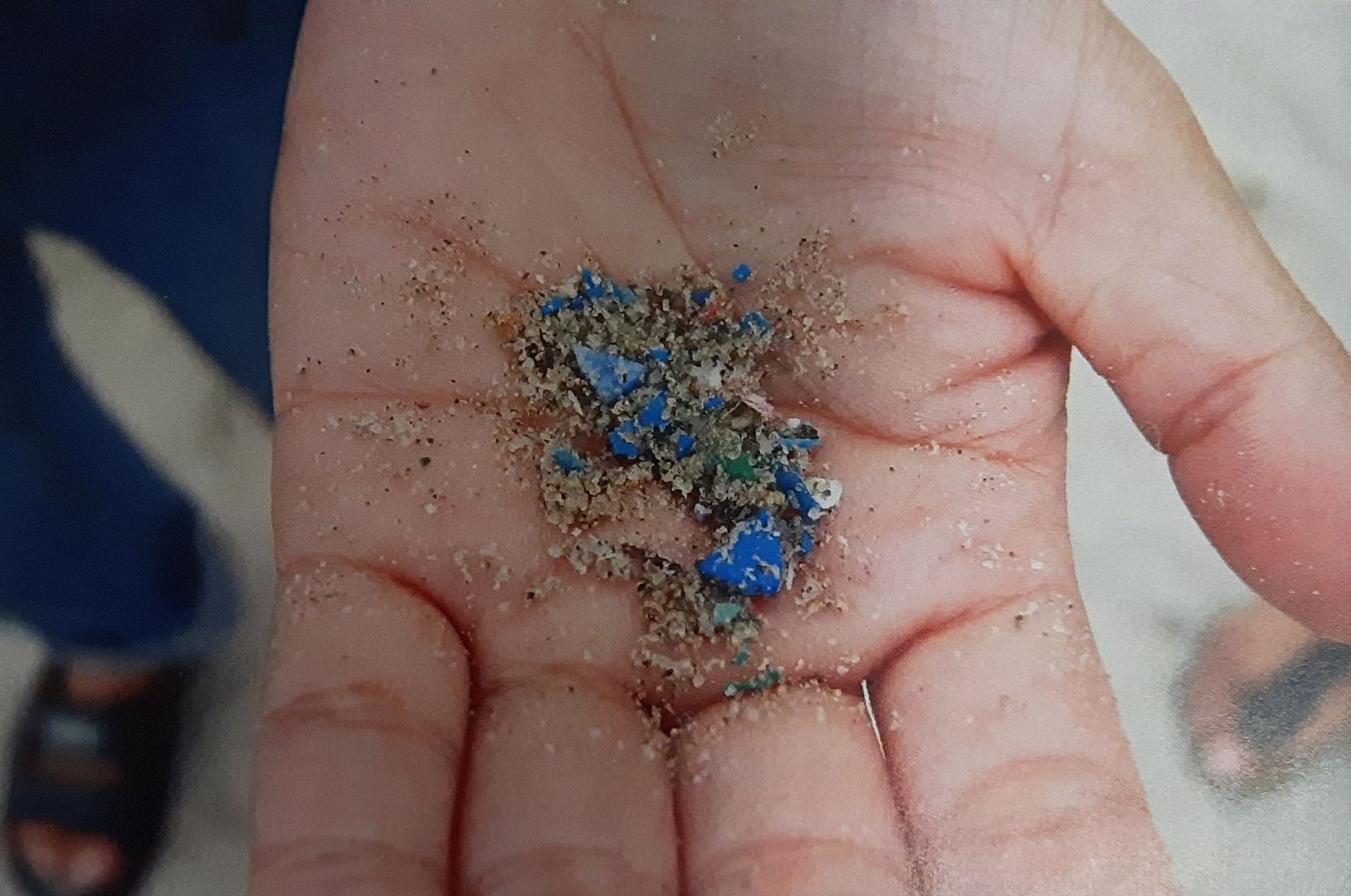 Zdjęcie przedstawia dłoń, na której znajduje się piasek morski z mikroplastikiem